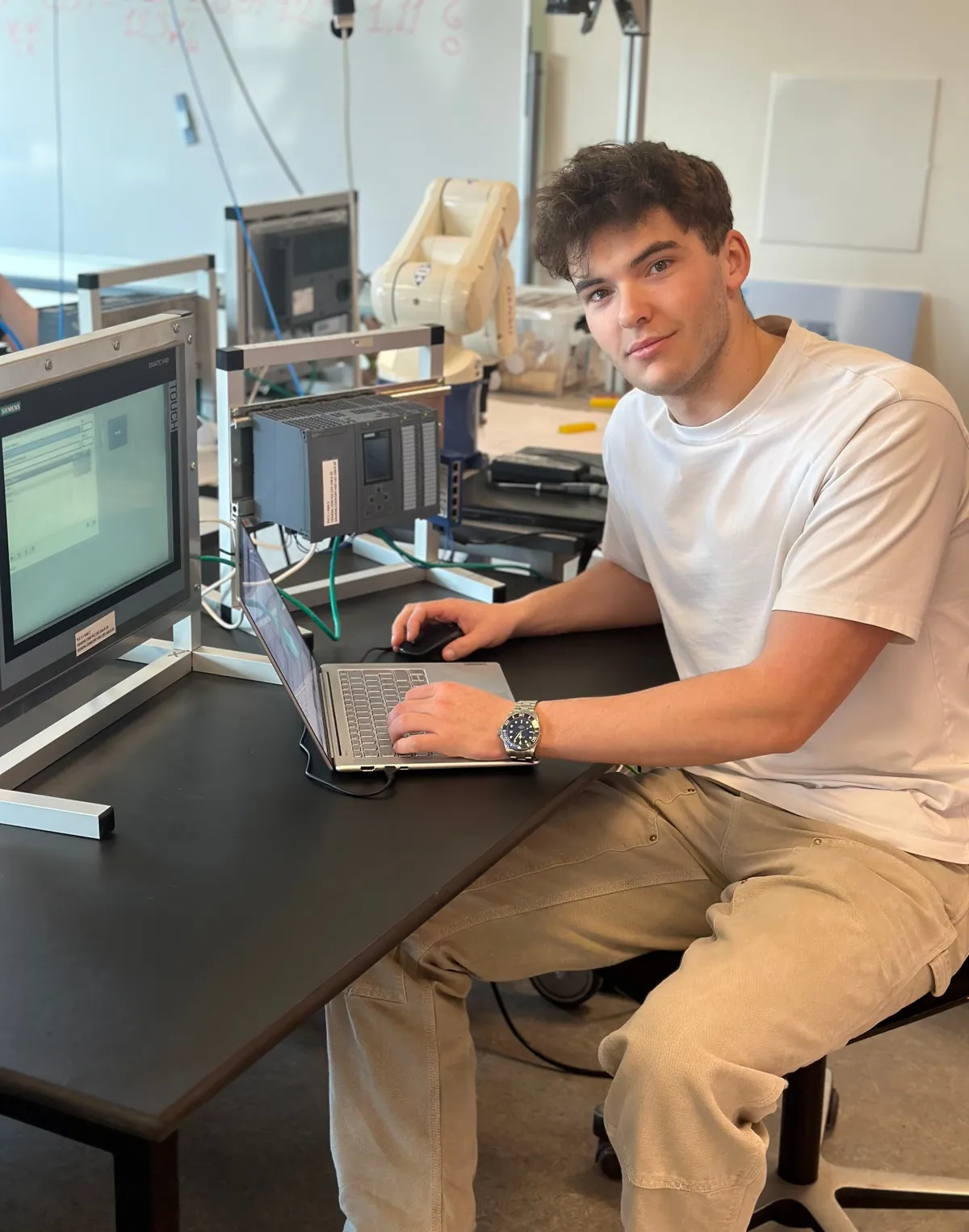 Oscar Ipsen arbejder ved computeren med PLC-system og robot i baggrunden